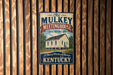 A vintage-style metal sign for the Old Mulkey Meetinghouse, a historic site in Kentucky, is displayed on a wooden wall.