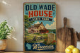 A vintage-style sign for Old Wade House State Park in Wisconsin, featuring a large illustration of a house surrounded by a wooden fence and a lake.