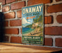 A vintage-style metal sign for Onaway State Park in Michigan, featuring a scenic landscape with a beach, mountains, and a lake.