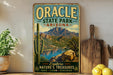 A vintage-style metal sign for Oracle State Park in Arizona, featuring a scenic mountain landscape with a lake and cactus in the foreground.