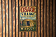 A vintage-style metal sign for the Osage Village State Historic Site in Missouri, featuring an illustration of a teepee and a wooden fence.