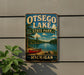 A metal sign with the text "OTSEGO LAKE STATE PARK MICHIGAN" and an illustration of a red canoe on a lake, mounted on a wall.