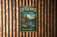 A vintage metal sign for Otter River State Forest in Massachusetts, featuring a scenic illustration of a forest and a river.