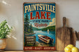 A vintage-style sign for Paintsville Lake State Park in Kentucky, featuring a scenic image of a lake with a boat, surrounded by nature and mountains.