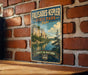 A vintage-style metal sign for Palisades-Kepler State Park in Iowa, featuring a scenic landscape with a lake and mountains.