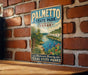 A vintage-style metal sign for Palmetto State Park, Texas, featuring a scenic landscape with palm trees, a river, and a desert landscape.