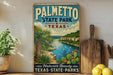 A vintage-style sign for Palmetto State Park, Texas, featuring a scenic landscape with palm trees, a river, and cacti.
