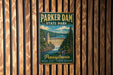 A vintage metal sign for Parker Dam State Park in Pennsylvania, featuring a scenic illustration of the dam and surrounding landscape.