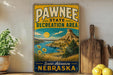 A vintage-style metal sign for the Pawnee State Recreation Area in Nebraska, featuring a scenic landscape with a mountain, lake, and sun.
