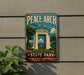 A vintage-style metal sign for Peace Arch State Park in Washington, featuring a white archway with a flag and a scenic landscape.