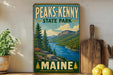 A vintage-style sign for Peaks- Kenny State Park in Maine, featuring a scenic landscape with mountains, pine trees, and a lake.