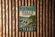 A vintage-style metal sign for Pedernales Falls State Park in Texas, featuring a scenic image of the waterfall surrounded by lush greenery.