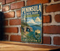 A vintage-style metal sign for Peninsula State Park in Wisconsin, featuring a scenic landscape with a lake, mountains, and a bridge.