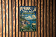 A vintage-style sign for Peninsula State Park in Wisconsin, featuring a scenic landscape with a lake, mountains, and a bridge.