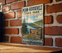 A vintage-style sign for Penn-Roosevelt State Park, featuring a scenic landscape with a lake and mountains, mounted on a brick wall.