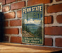 A vintage-style metal sign for Penn State Forest, featuring a scenic mountain landscape with pine trees and a lake.