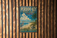 A vintage-style metal sign for Perdido Key State Park, Florida, featuring a seagull, palm tree, and ocean waves, mounted on a wooden fence.