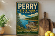 A vintage-style metal sign for Perry State Park in Kansas, featuring a scenic landscape with a lake, mountains, and a wooden signpost.