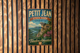 A vintage-style metal sign for Petit Jean State Park in Arkansas, featuring a scenic landscape with a cliff and river.