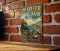 A vintage-style metal sign for Pfeiffer Big Sur State Park, featuring a scenic coastal landscape with mountains, water, and a beach.