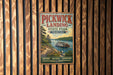 A vintage-style metal sign for Pickwick Landing State Park in Tennessee, featuring a scenic illustration of a riverboat on a wooden bridge surrounded by trees.