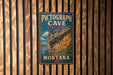 A vintage metal sign for Pictograph Cave State Park in Montana, featuring an illustration of a cave with rock art.