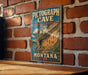 A vintage-style sign for Pictograph Cave State Park in Montana, featuring a scenic illustration of the cave and its surroundings.
