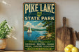 A vintage-style sign for Pike Lake State Park in Ohio, featuring a scenic illustration of a lake with a sailboat, surrounded by nature and outdoor activities.