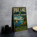 A vintage-style metal sign for Pike Lake State Park, featuring a scenic illustration of a lake, sailboat, and mountains.