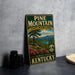 A vintage-style metal sign for Pine Mountain State Resort Park in Kentucky, featuring a scenic landscape with a pine tree, mountains, and a lake.