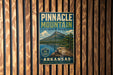 A vintage-style metal sign for Pinnacle Mountain State Park in Arkansas, featuring a scenic mountain landscape with a lake and pine trees.