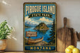A vintage-style sign for Pirogue Island State Park in Montana, featuring a scenic illustration of the island surrounded by mountains and a lake.