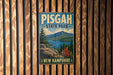 A vintage metal sign for Pisgah State Park in New Hampshire, featuring a scenic mountain landscape with a lake and pine trees.