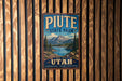 A vintage-style metal sign for Piate State Park, featuring a mountain landscape and a lake, is displayed on a wooden wall.