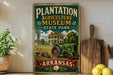 A vintage-style sign for the Plantation Agriculture Museum in Arkansas, featuring an illustration of a house, windmill, and tractor in a rural setting.