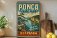 A vintage-style poster of Pona State Park in Nebraska, featuring a scenic landscape with a river and cliffs, is displayed on a wall next to a wooden cutting board and some kitchen utensils.