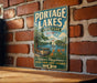 A vintage-style metal sign for Portage Lakes State Park, Ohio, featuring a scenic illustration of a lake, a sailboat, and a wooden dock.