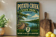 A vintage-style sign for Potato Creek State Park in Indiana, featuring a scenic image of a wooden boardwalk and a river, along with the words "Potato Creek State Park Indiana" and "Explore Nature History Adventure".