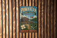 A vintage-style metal sign for Powhatan Historic State Park in Arkansas, featuring a wooden cabin and a flag, is displayed on a wooden wall.