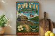a vintage-style sign for Powhatan Historic State Park in Arkansas, with a wooden cabin and a river in the background. The sign is displayed on a shelf next to a wooden cutting board and a potted plant.