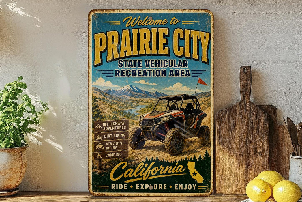 a vintage-style metal sign that reads "Welcome to Prairie City State Vehicular Recreation Area" with an illustration of an off-road vehicle in the background.