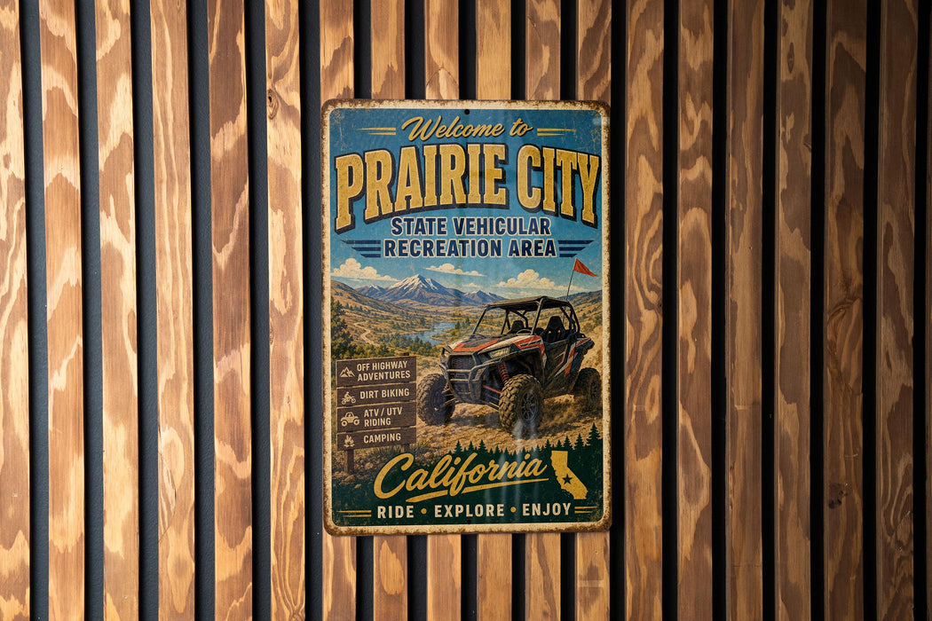 A vintage metal sign welcoming visitors to Prairie City, featuring an illustration of a vehicle and a scenic landscape.