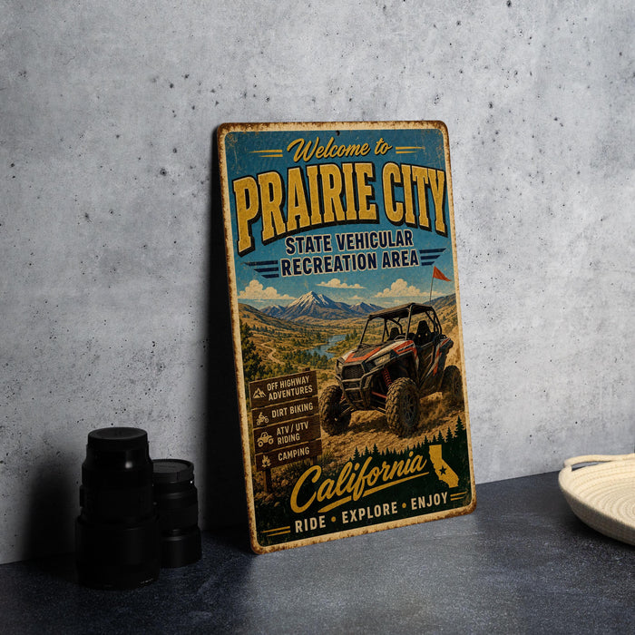 a vintage metal sign for Prairie City State Vehicular Recreation Area, with a colorful illustration of a dirt bike and mountains in the background.