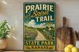 A vintage-style sign for the Prairie Spirit Trail in Kansas, featuring a scenic countryside landscape with a dirt path and a wooden fence.
