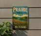 A vintage-style metal sign for Prairie State Park in Missouri, featuring a scenic landscape with a river, grass, and flowers.