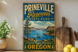 A vintage-style sign for Prineville Reservoir State Park, featuring a scenic landscape with a lake, mountains, and a boat.