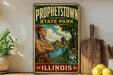 A vintage-style sign for "Prophetstown State Park" in Illinois, featuring an illustration of a Native American man with a bird perched on his head. The sign is displayed on a shelf next to a wooden cutting board and some lemons.