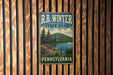 A vintage-style metal sign for R.B. Winter State Park in Pennsylvania, featuring a scenic landscape with a lake, mountains, and a sailboat.