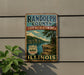 A vintage metal sign for the Randolph County State Recreation Area in Illinois, featuring a scenic landscape with a lake and mountains.