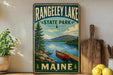 A vintage-style sign for Rangeley Lake State Park in Maine, featuring a scenic image of a lake, mountains, and a canoe.